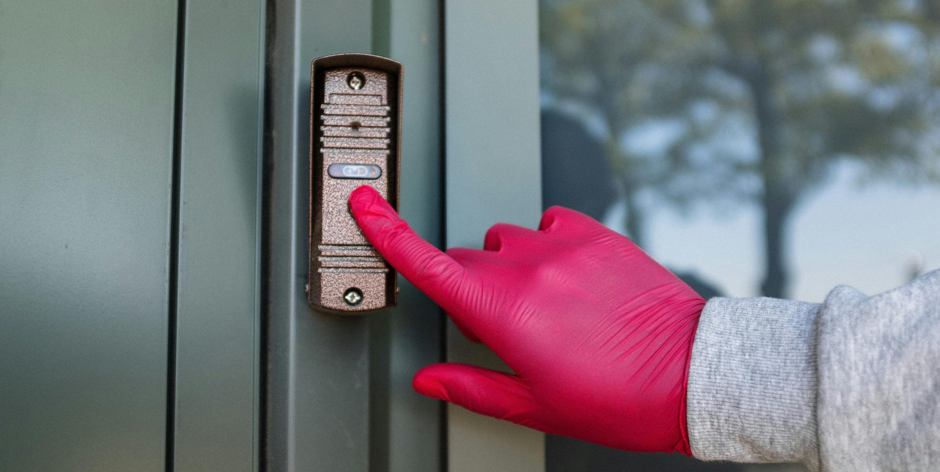 A red gloved hand presses a modern doorbell on a metal door, depicting security and service.
